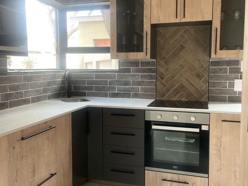 Modern kitchen featuring wood-tone cabinetry, stone countertops, a herringbone tile backsplash, and integrated appliances including an oven and electric hob.
