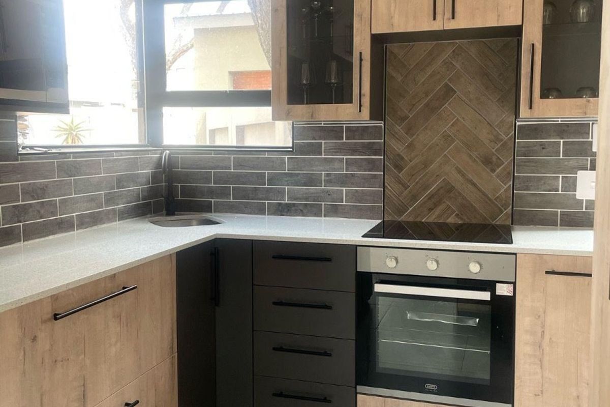 Modern kitchen featuring wood-tone cabinetry, stone countertops, a herringbone tile backsplash, and integrated appliances including an oven and electric hob.