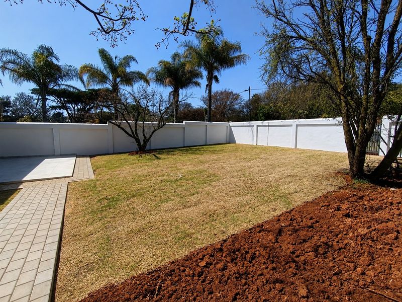 A spacious rear garden featuring a well-maintained perimeter wall, paved walkway, and a tiled patio area, offering a clean outdoor space.