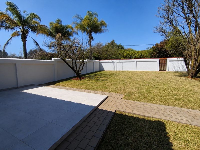 A well-maintained rear garden featuring a paved patio area, a brick walkway, and a secure perimeter wall with a gate.