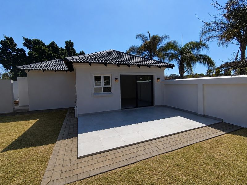 A well-maintained rear exterior view of the cottage featuring a clean tiled patio, sliding glass doors, and a surrounding boundary wall.