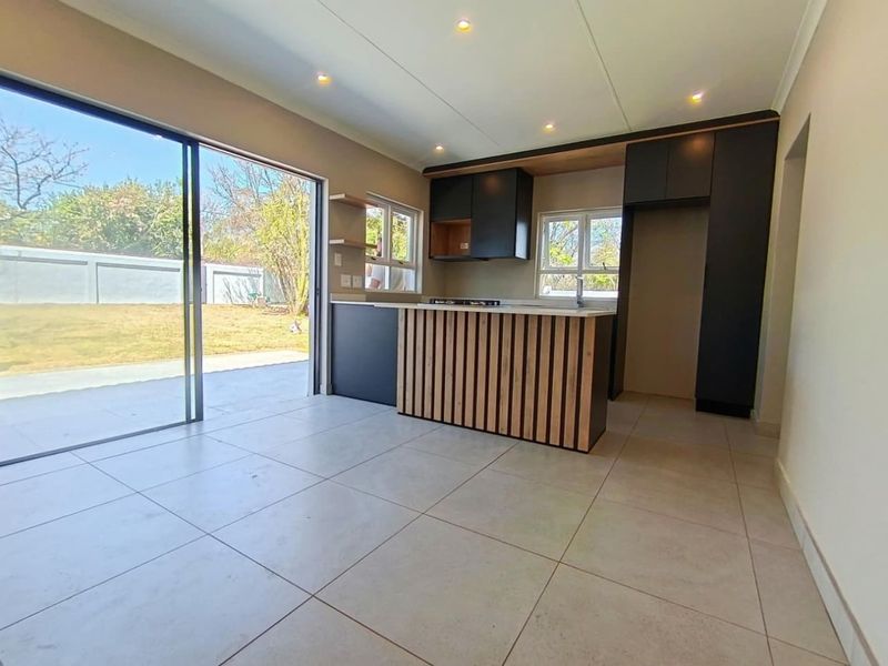 Modern kitchen featuring dark cabinetry, a slatted wood-accented island, tiled flooring, and large sliding doors providing direct access to the rear garden.