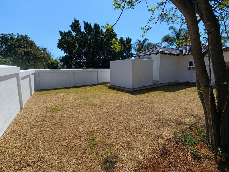 A private rear garden featuring a well-maintained boundary wall, a tiled roof cottage extension, and established trees.