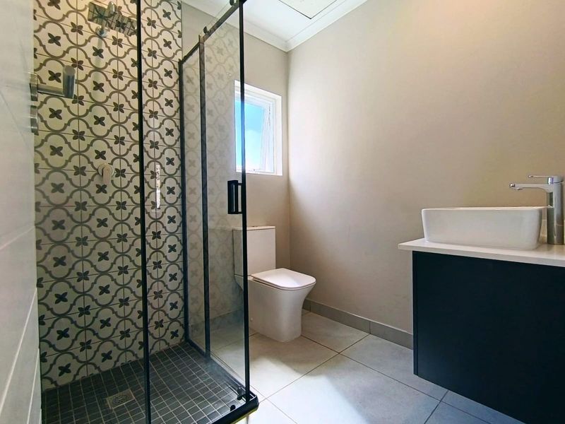 Modern bathroom featuring a walk-in shower with patterned tile accents, a sleek vanity with a vessel sink, and a contemporary toilet.