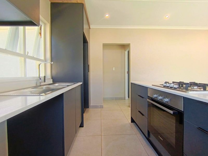 Modern kitchen featuring sleek dark cabinetry, stone countertops, integrated stainless steel oven, gas hob, and tiled flooring in a clean, contemporary layout.