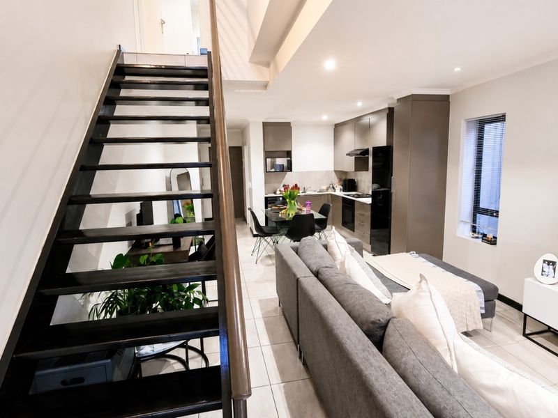 Modern open-plan living area featuring a sleek staircase, tiled flooring, and a contemporary kitchen with integrated cabinetry and built-in appliances.