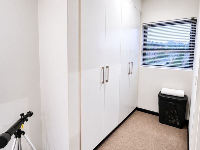A clean, minimalist bedroom featuring floor-to-ceiling built-in cupboards and a window with venetian blinds, offering a bright and neutral space.