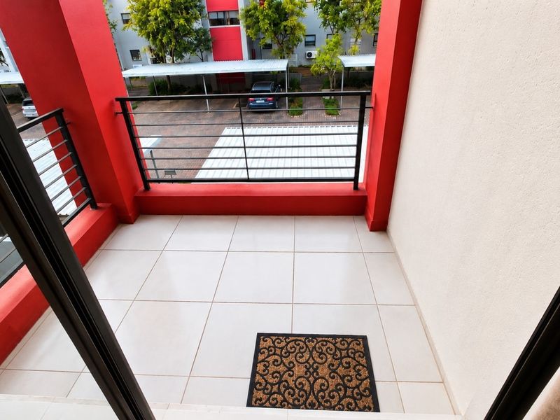A clean, covered balcony featuring tiled flooring and a metal balustrade, overlooking the complex parking area.