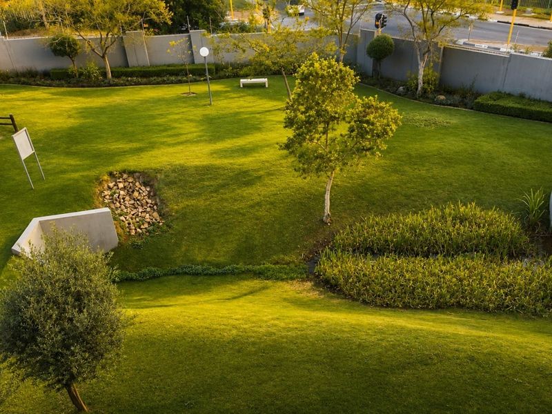 An elevated view of a well-maintained landscaped garden featuring manicured lawns, stone drainage elements, and perimeter boundary walls.
