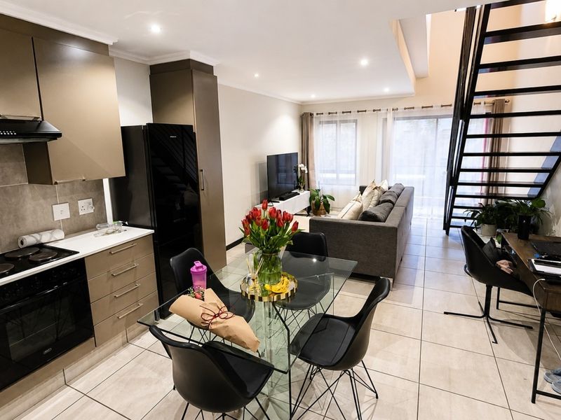 Modern open-plan living area featuring a contemporary kitchen with built-in appliances, tiled flooring, and a striking metal staircase leading to the upper level.