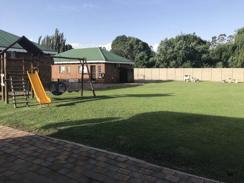 Spacious backyard featuring a large manicured lawn, paved patio area, and a secure precast concrete boundary wall.