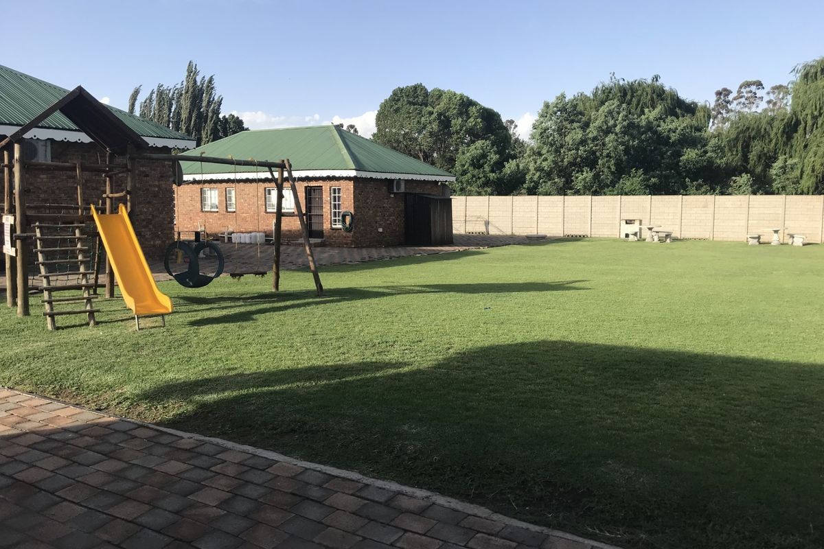Spacious backyard featuring a large manicured lawn, paved patio area, and a secure precast concrete boundary wall.