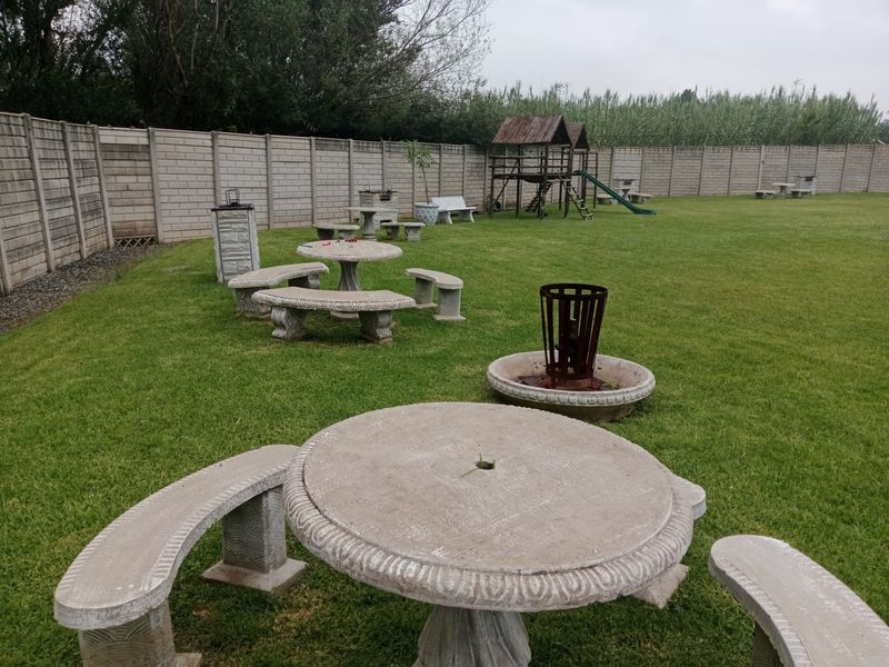 Spacious backyard garden featuring a large lawn, precast concrete boundary walls, and various fixed concrete seating areas with a children's play structure.