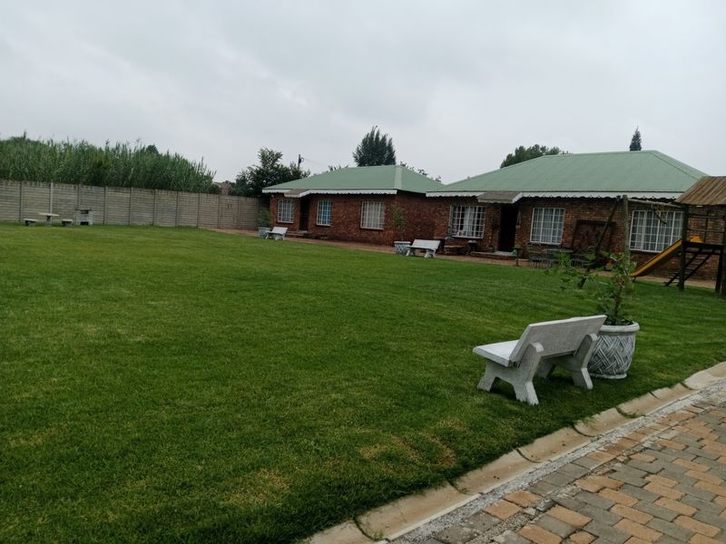 Spacious rear garden featuring a large lawn, brick-built house with green metal roofing, and secure boundary walling.