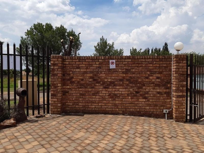 A secure front entrance featuring a sturdy brick boundary wall, metal security gate, and paved driveway area.