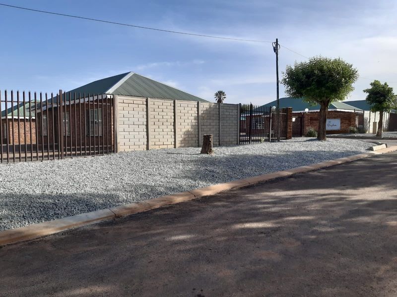 Street view of the property featuring brick exterior walls, corrugated metal roofing, and secure perimeter fencing with gravel landscaping.
