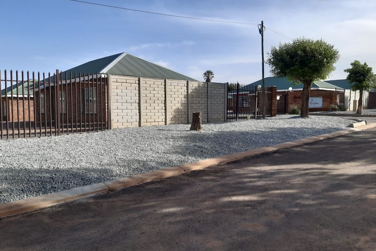 Street view of the property featuring brick exterior walls, corrugated metal roofing, and secure perimeter fencing with gravel landscaping.