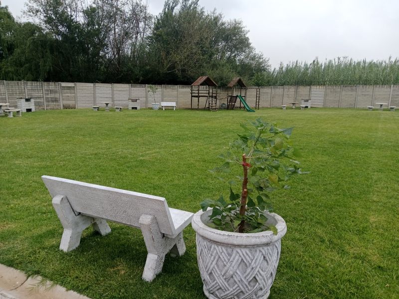A spacious, well-maintained garden featuring a large lawn area enclosed by a precast concrete boundary wall with fixed concrete seating.