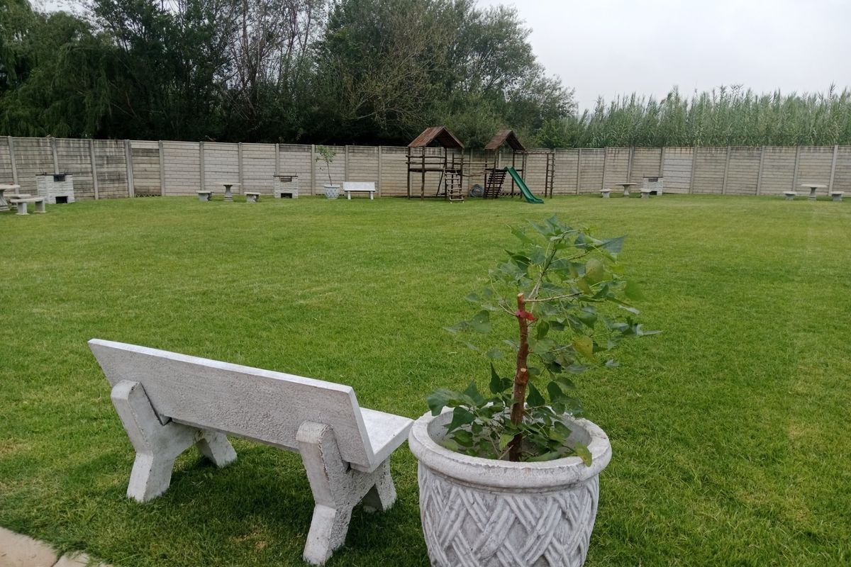 A spacious, well-maintained garden featuring a large lawn area enclosed by a precast concrete boundary wall with fixed concrete seating.