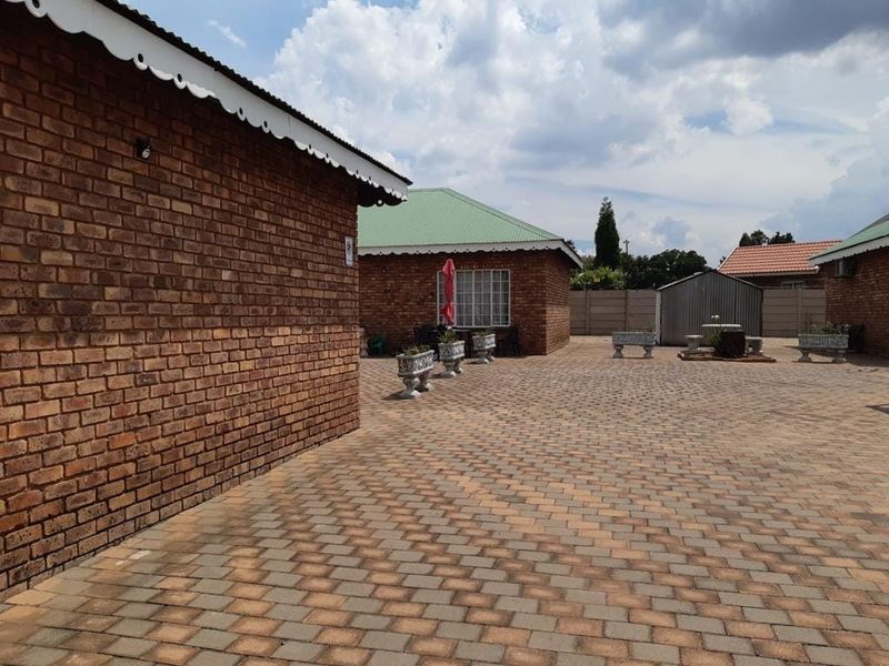 A spacious paved rear courtyard area featuring face-brick building exteriors, a metal storage shed, and perimeter precast concrete walling.