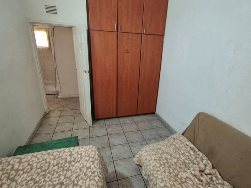 A bedroom featuring tiled flooring and a built-in wooden wardrobe, with an adjacent room visible through the doorway.
