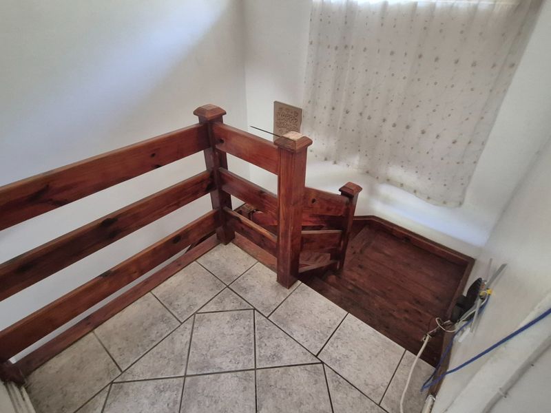 A staircase landing area featuring a wooden balustrade and tiled flooring, showing signs of dated finishes and exposed wiring.