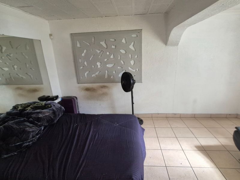 A bedroom featuring tiled flooring, a large wall-mounted mirror, and a decorative wall panel, showing signs of wear and wall staining.