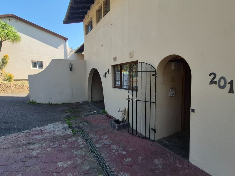 Front entrance view of the property featuring an arched doorway, security gate, and paved driveway area.
