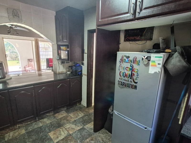 A dated kitchen featuring dark wood cabinetry, granite countertops, and tiled flooring, with an open archway leading to an adjacent living area.