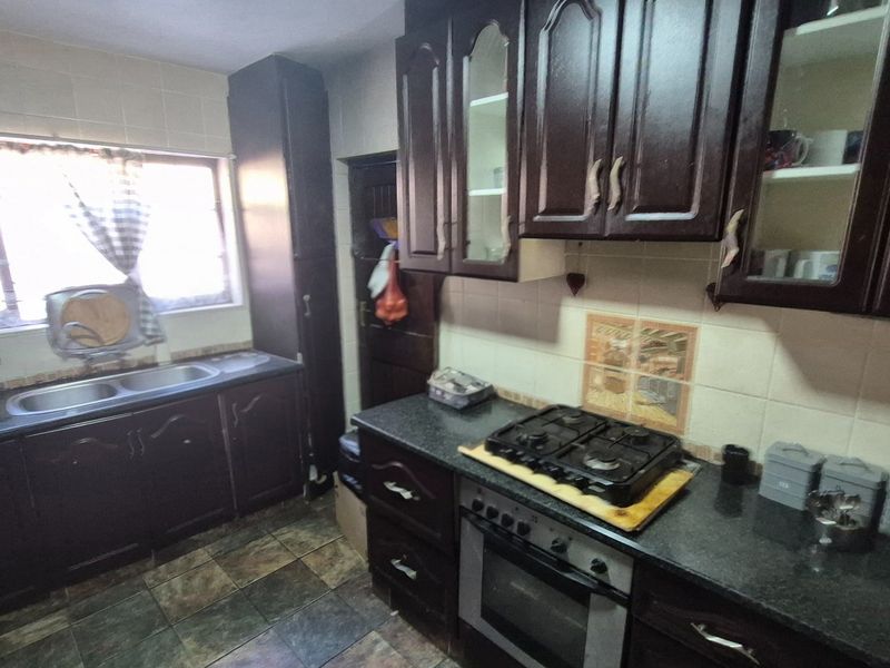 A functional kitchen featuring dark wood cabinetry, a built-in oven with gas hob, double basin sink, and tiled finishes throughout.
