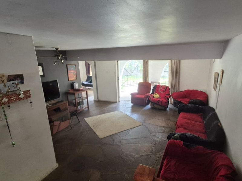 A living room featuring rustic stone flooring, a ceiling fan, and an archway leading to an outdoor area.