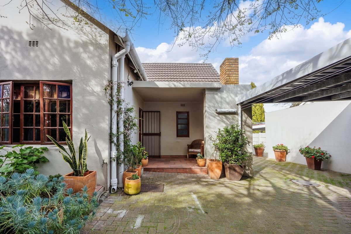 Rear exterior view featuring a covered tiled patio, paved driveway area, and a carport structure attached to the main dwelling.