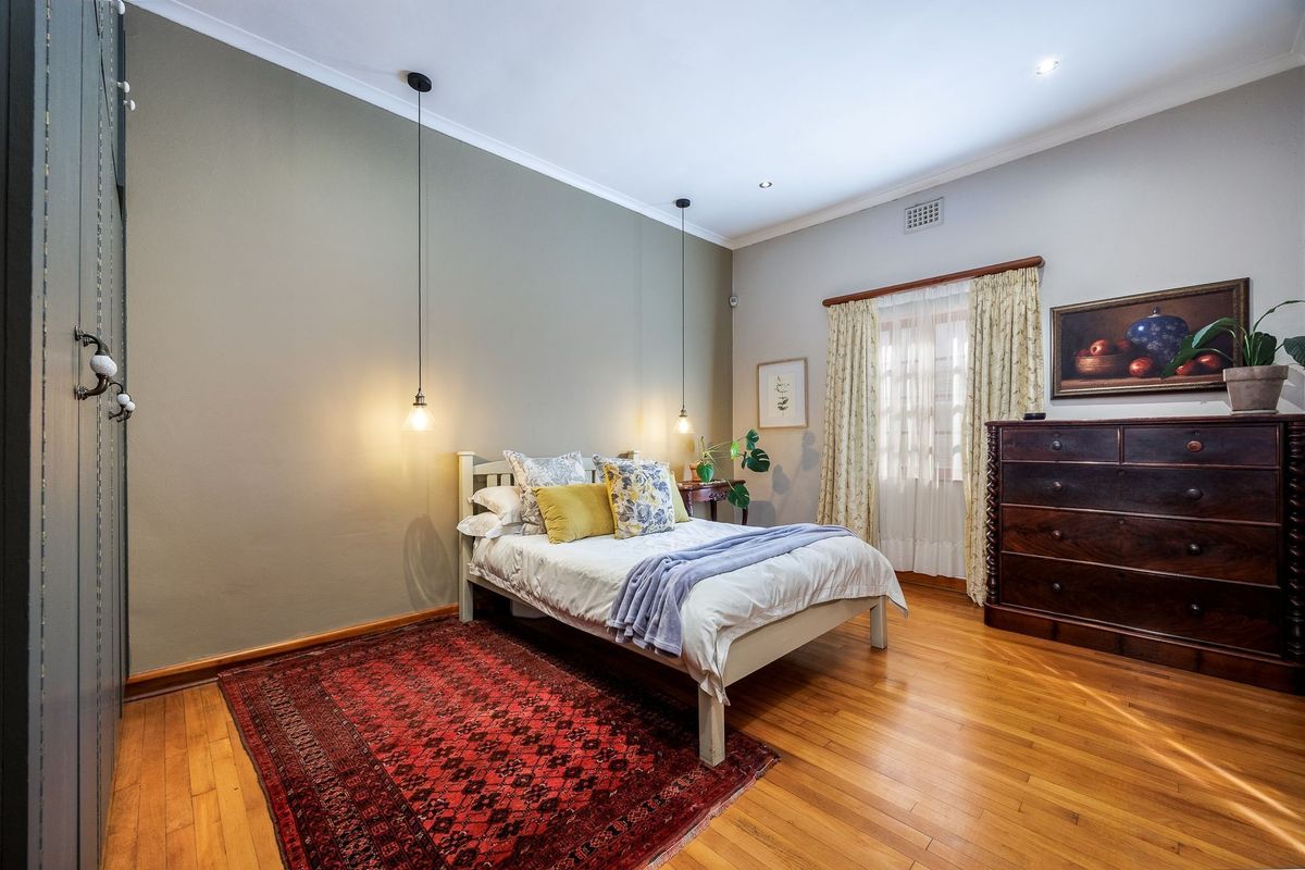 A well-maintained bedroom featuring polished hardwood flooring, built-in cabinetry, elegant pendant lighting, and classic cornicing details.
