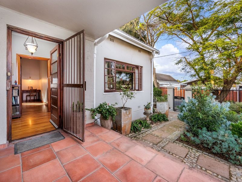 A charming covered patio featuring terracotta tiling, a secure entrance gate, and direct access to a landscaped garden and paved walkway.