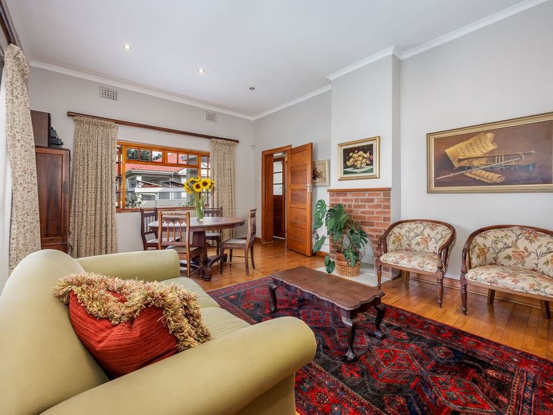 A well-maintained living room featuring hardwood flooring, a classic brick fireplace, and natural light through timber-framed windows.