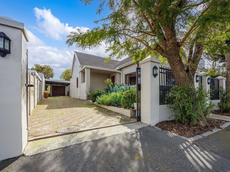 Front view of the property featuring a paved driveway, secure boundary wall with wrought iron gate, and a covered carport.