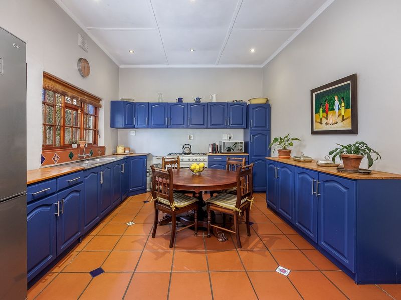 A spacious kitchen featuring vibrant blue cabinetry, warm wooden countertops, terracotta flooring, and a functional gas stove setup.