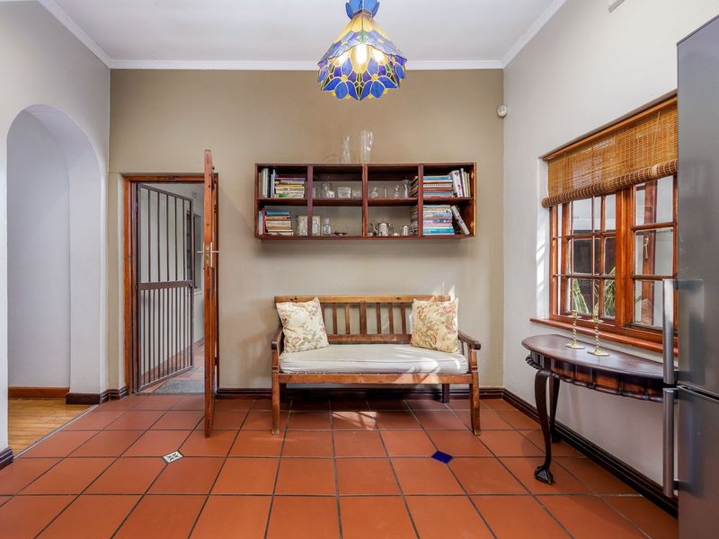 A living area featuring terracotta tiled flooring, an arched entryway, wooden window frames, and built-in wall shelving.