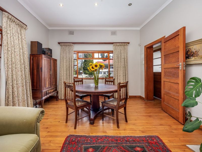 A well-maintained dining room featuring warm hardwood flooring, classic timber door frames, and a brick fireplace, offering a cozy and traditional atmosphere.