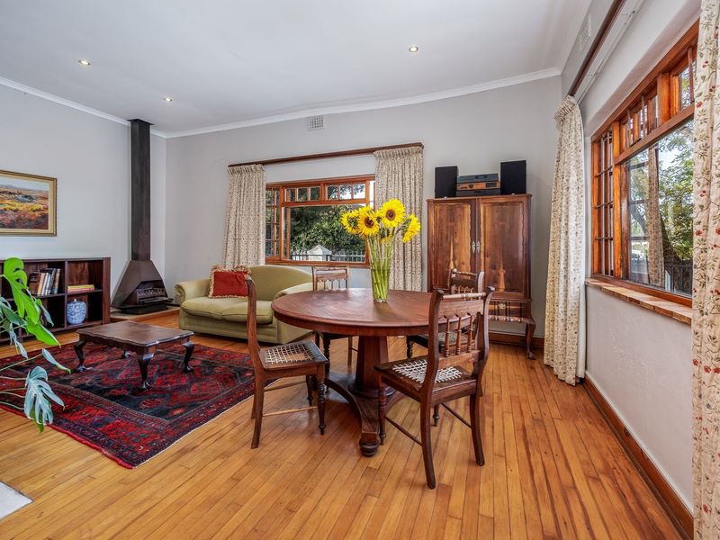 Spacious living area featuring warm hardwood flooring, a classic freestanding fireplace, and large timber-framed windows that provide ample natural light.