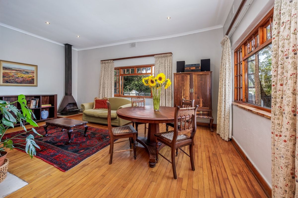 Spacious living area featuring warm hardwood flooring, a classic freestanding fireplace, and large timber-framed windows that provide ample natural light.