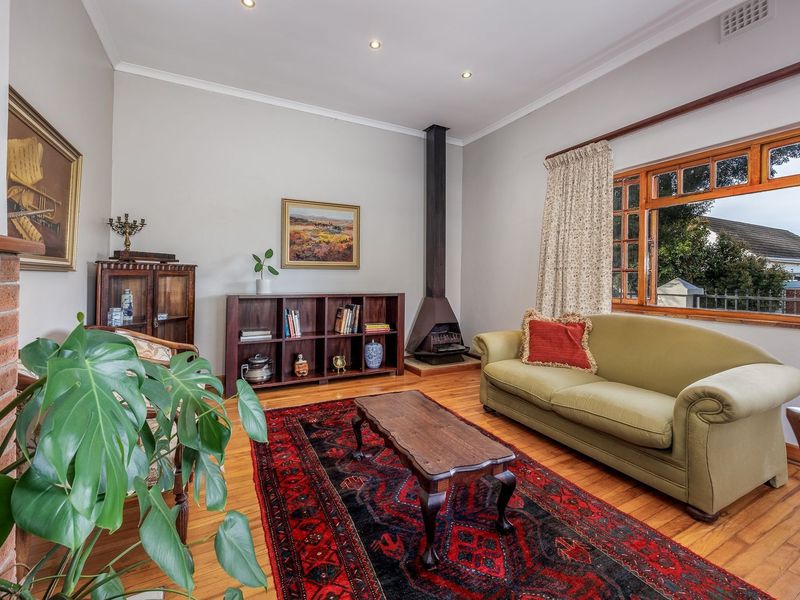 A well-maintained living room featuring polished timber flooring, a prominent freestanding fireplace, and large timber-framed windows providing natural light.