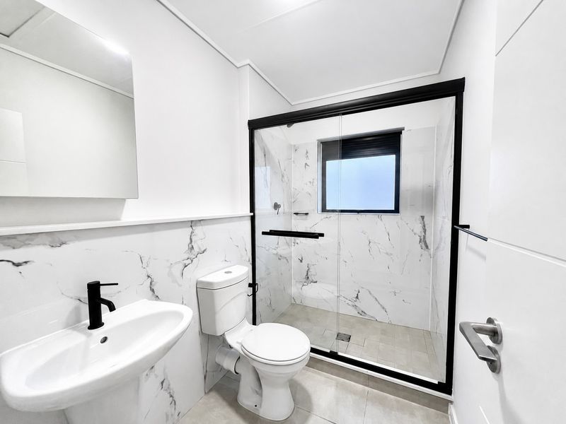 Modern bathroom featuring marble-look wall tiles, a walk-in shower with a black-framed glass screen, a wall-mounted basin, and a contemporary toilet.