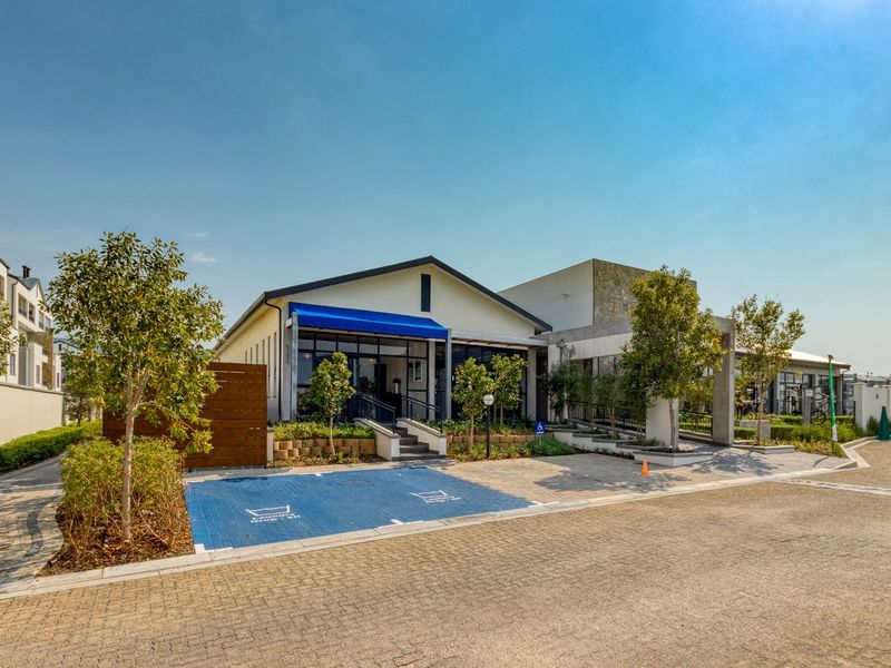 Exterior view of the modern apartment complex clubhouse featuring stone accents, a blue awning, and dedicated parking facilities within a landscaped setting.