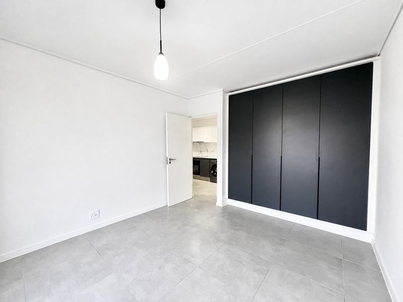 A bright, modern bedroom featuring large matte black built-in wardrobes, neutral grey floor tiles, and a minimalist pendant light fixture.