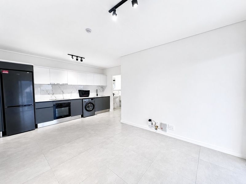 Modern open-plan kitchen featuring sleek two-tone cabinetry, integrated appliances, marble-look splashback, and contemporary track lighting in a bright, tiled living space.