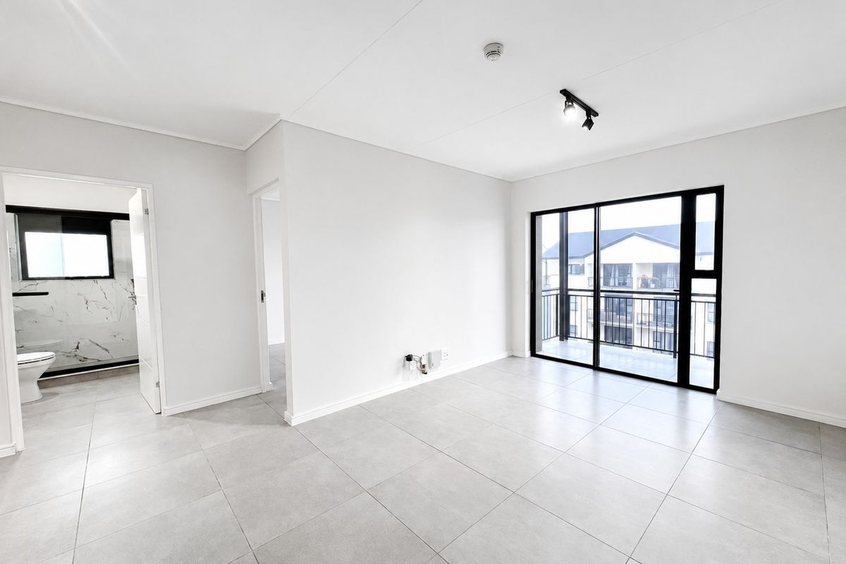 A bright, open-plan living area featuring modern tiled flooring, track lighting, and a large sliding glass door leading to a balcony.