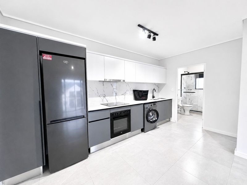 Modern kitchen featuring sleek grey and white cabinetry, marble-look splashback, integrated appliances, and contemporary track lighting, with an adjacent bathroom visible.