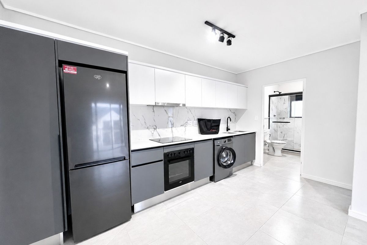 Modern kitchen featuring sleek grey and white cabinetry, marble-look splashback, integrated appliances, and contemporary track lighting, with an adjacent bathroom visible.