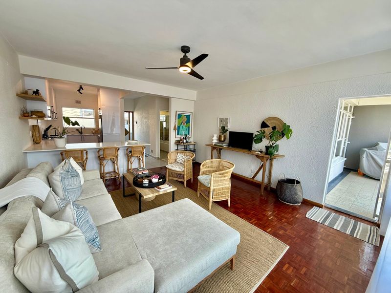 Open-plan living area featuring warm parquet flooring, a modern ceiling fan, and a breakfast bar connecting to the kitchen space.